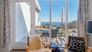 Una habitación con un ventanal grande que da a un patio con mobiliario exterior y vistas al mar.