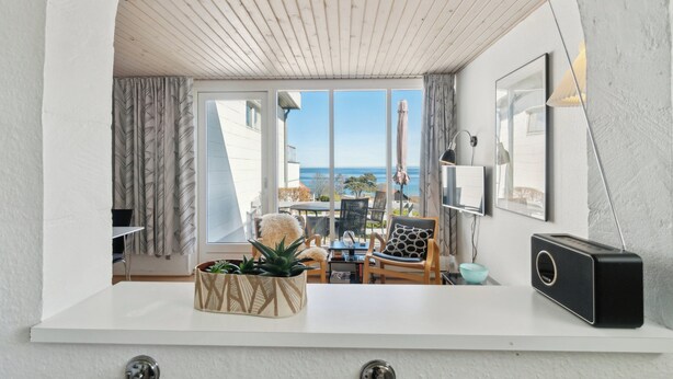 Un interior moderno con techo blanco, vistas al mar, una encimera blanca, un radio negro y una planta en una maceta geométrica.