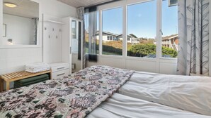 Un dormitorio con una cama grande, un armario, un espejo y una ventana con vistas a casas.