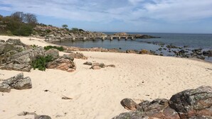 Una playa con costa rocosa, un muelle de hormigón y agua tranquila.