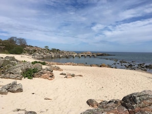 A beach with a rocky shoreline, a concrete pier, and calm water.