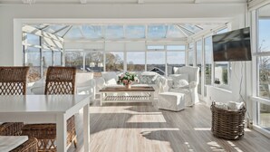A sunlit room with a large window, wicker furniture, a white sofa, and a wooden coffee table. - Lovely summer house with sea view (Sjølund)