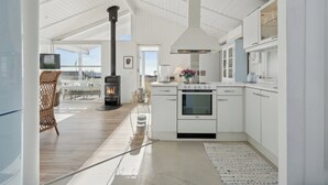 A modern kitchen with white cabinetry, a built-in stove, and a large window overlooking a deck. - Lovely summer house with sea view (Sjølund)