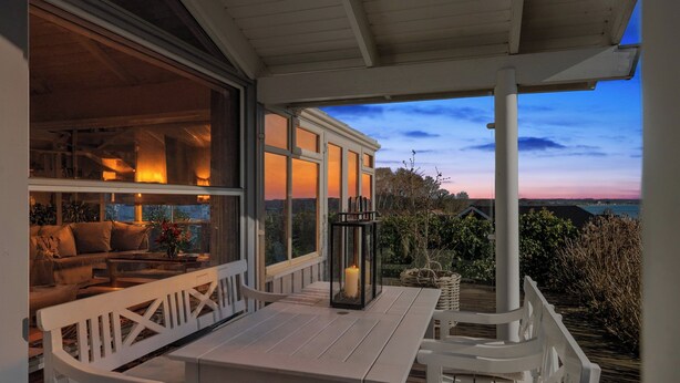 A covered outdoor seating area with a table and chairs, a lantern, and a view of the landscape. - Lovely summer house with sea view (Sjølund)