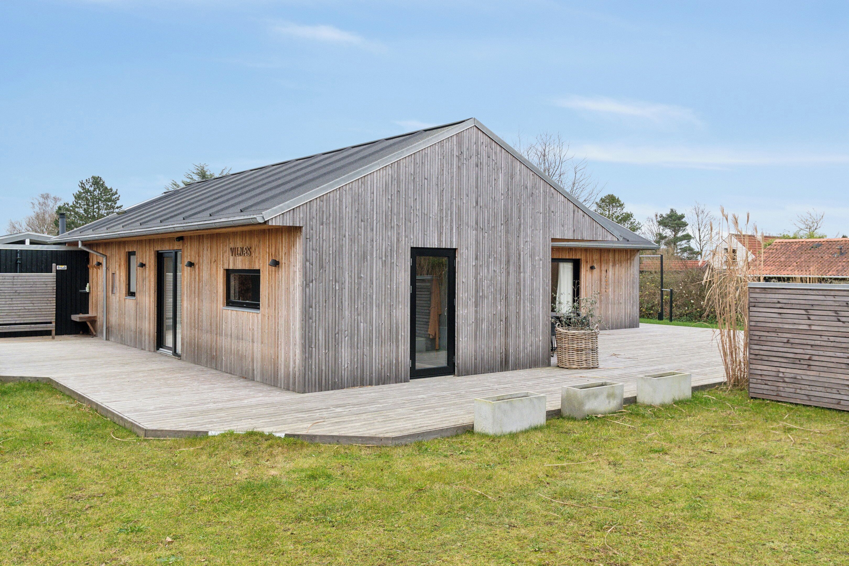 A modern wooden building with a sloped roof, a covered patio, and a small garden area.