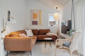 Un salon moderne comprenant un canapé, un fauteuil, une petite table, une lampe suspendue et un téléviseur.