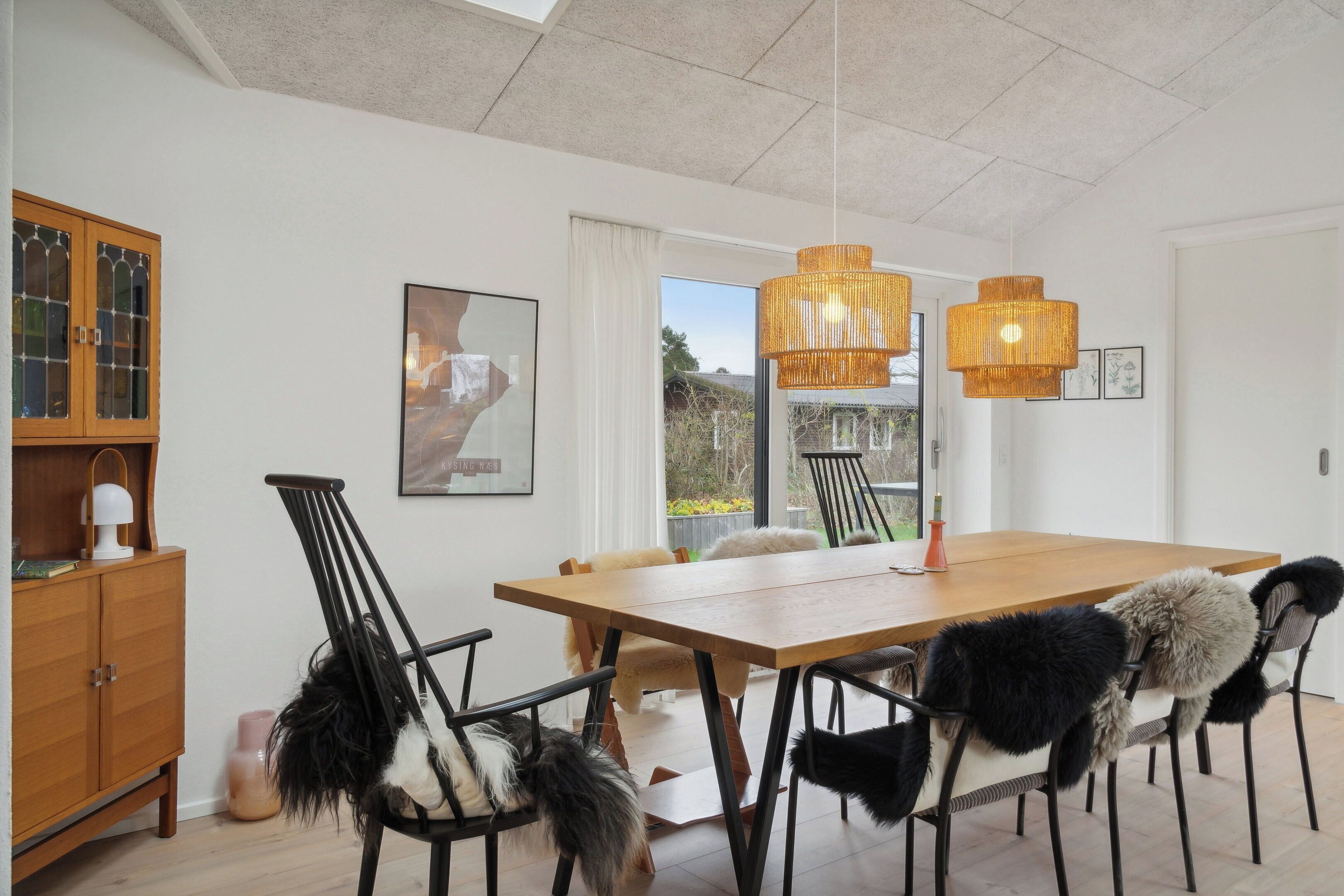 A dining area with a wooden table, black chairs with fur throws, and a hanging light fixture.
