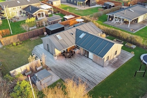 Une maison moderne dotée d’une grande terrasse, d’un espace salon extérieur abrité et d’une pelouse bien entretenue.