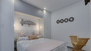 A bedroom with a bed, two nightstands, a wall-mounted shelf, and a wooden chair. - Bellavista Studio (Albufeira)