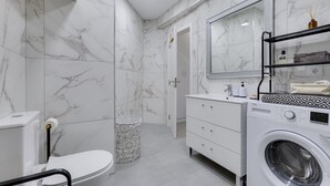 A modern bathroom with a toilet, sink, mirror, and washing machine. - Bellavista Studio (Albufeira)