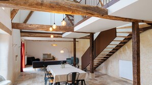 A spacious dining area with a high ceiling and exposed wooden beams, a staircase leading to an upper level, and a view of the dining area from the staircase. - In the heart of the Gers countryside, discover the Gîte Laborde (Monpardiac)