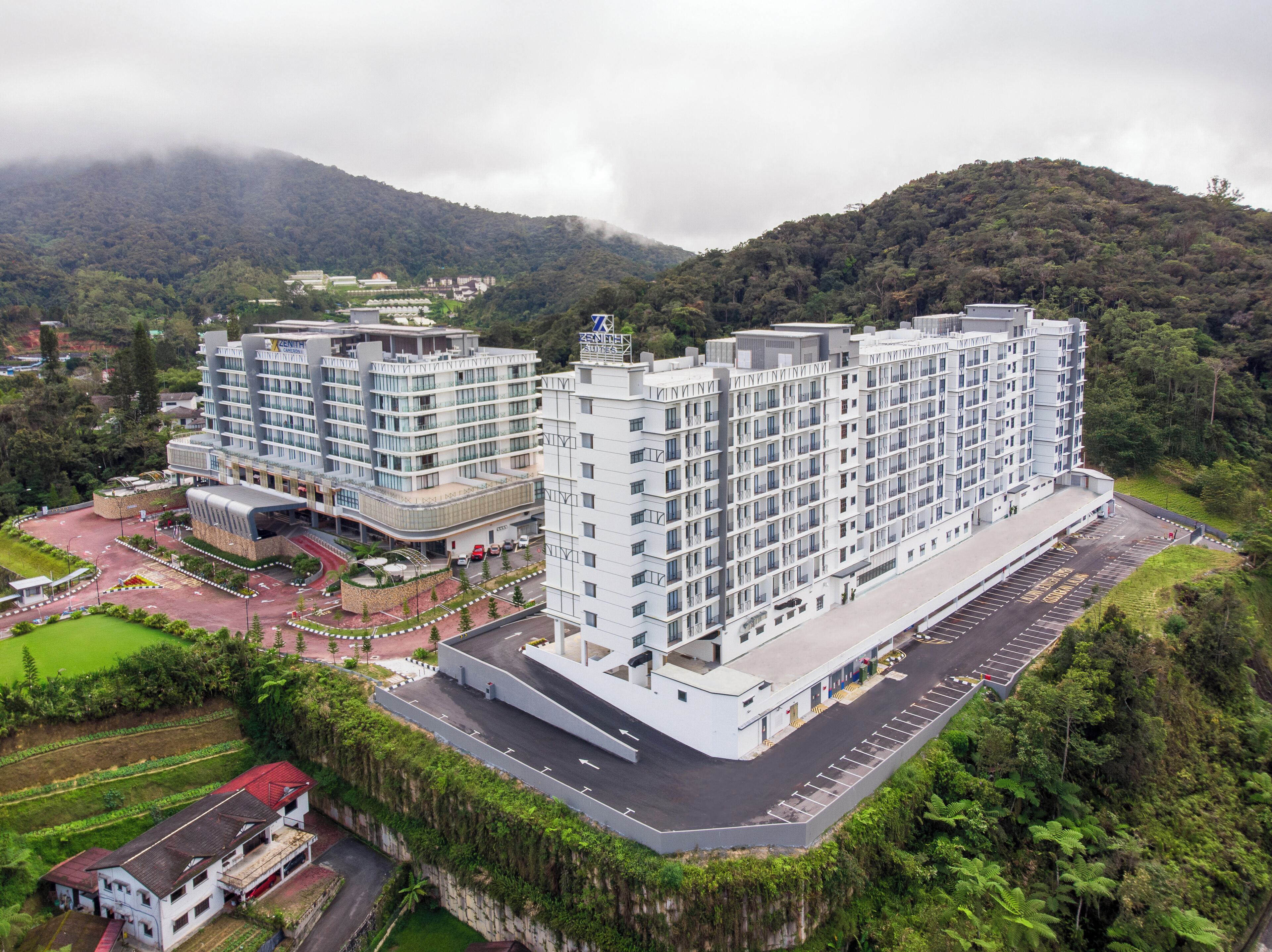 Un hotel moderno con varios pisos, una zona de estacionamiento y un jardín ajardinado.
