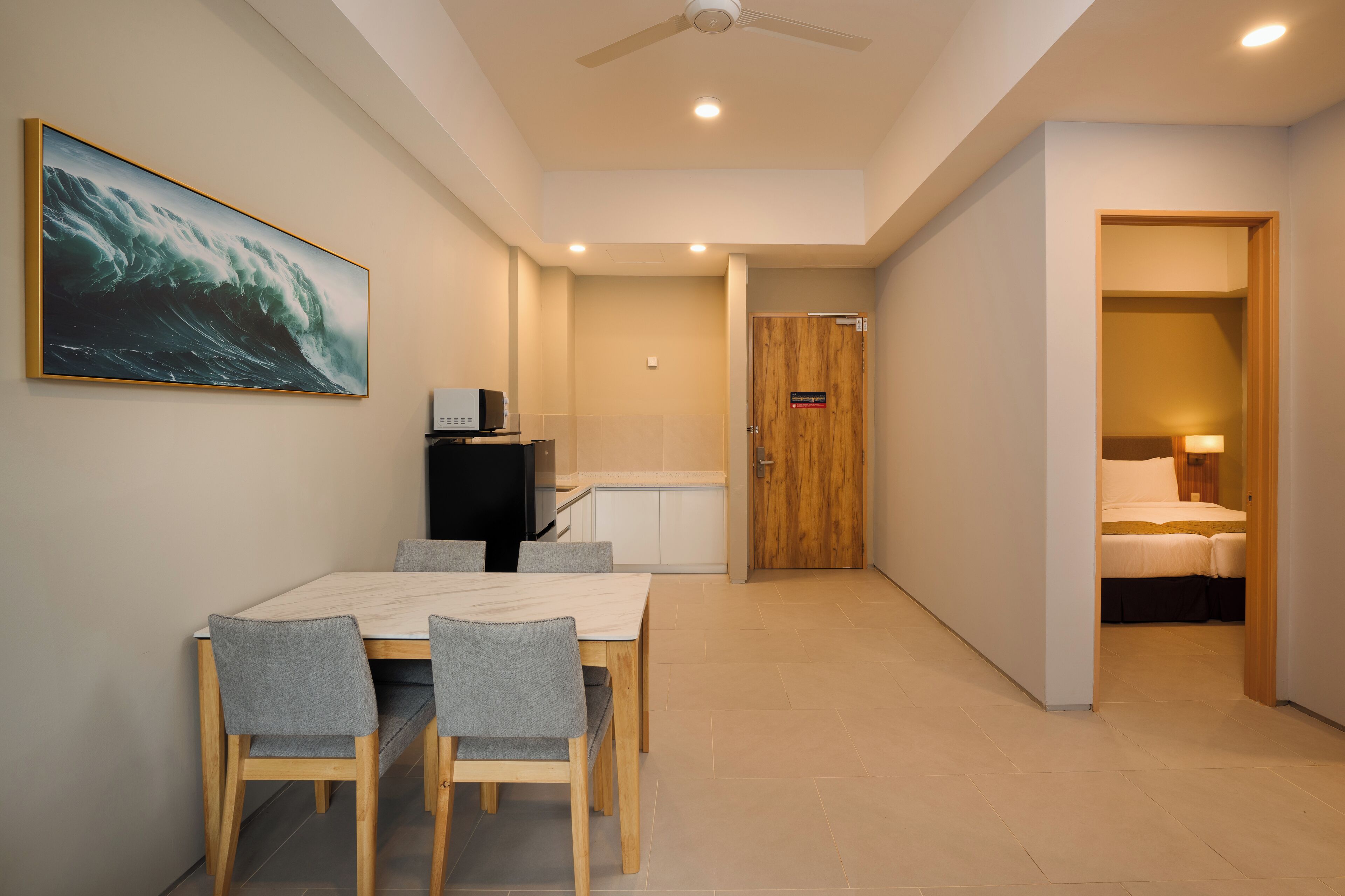 Une chambre d’hôtel avec un lit, un bureau et une chaise. On y trouve une porte qui donne sur une autre pièce, et la chambre offre une vue sur le couloir.