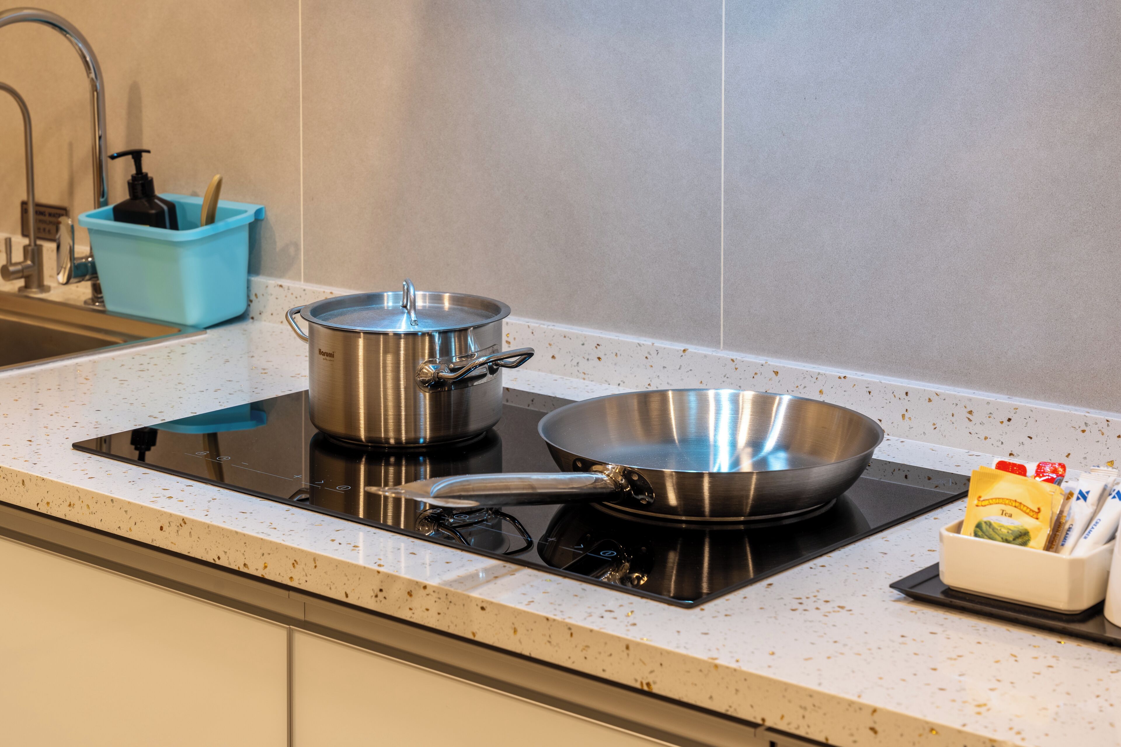 Una cocina con estufa, dos ollas, una sartén y un mueble para especias.