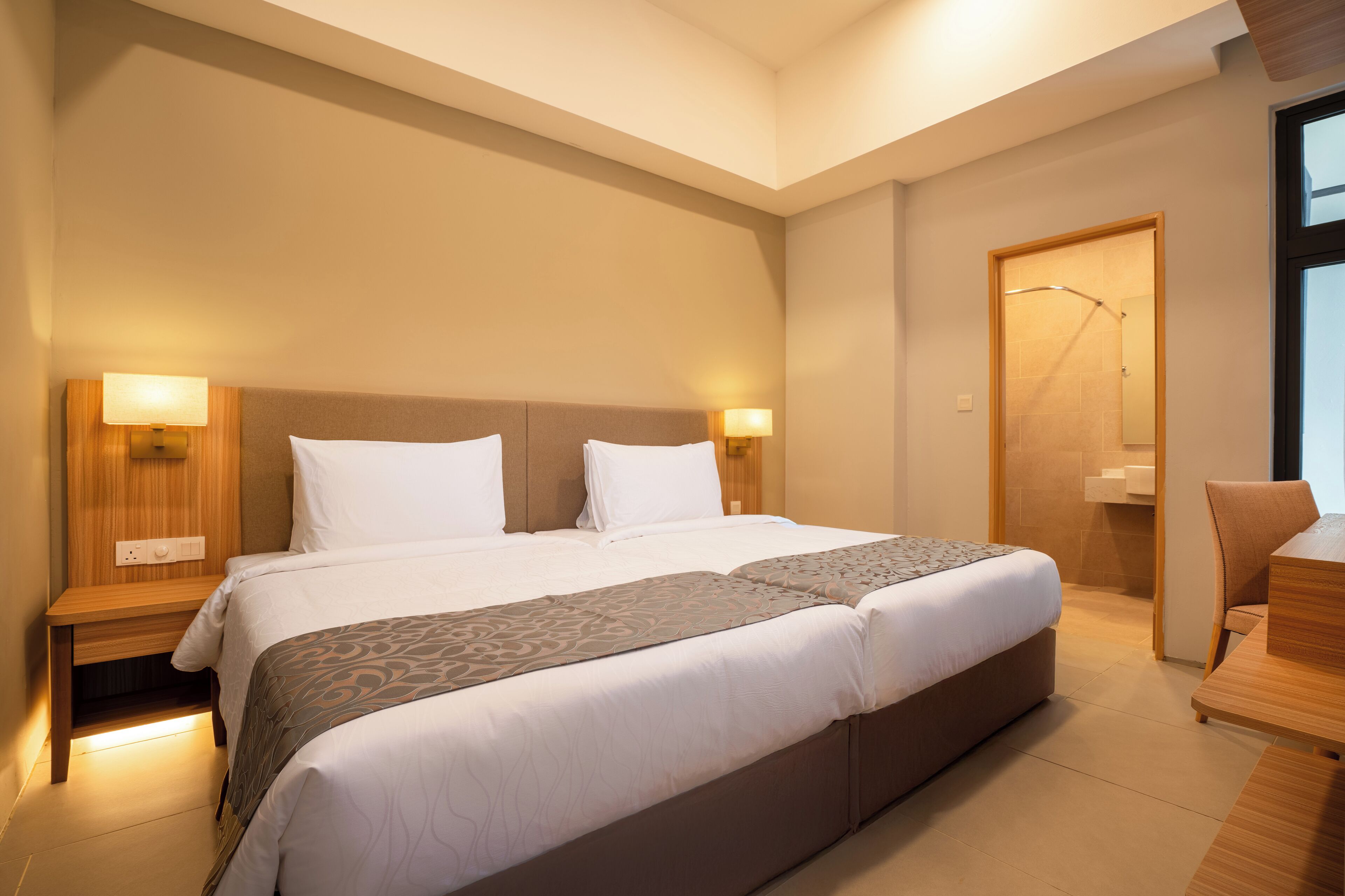 Ein modernes Hotelzimmer mit einem großen Bett, zwei Nachttischen mit Lampen, einem Holztisch und einem Duschbereich.