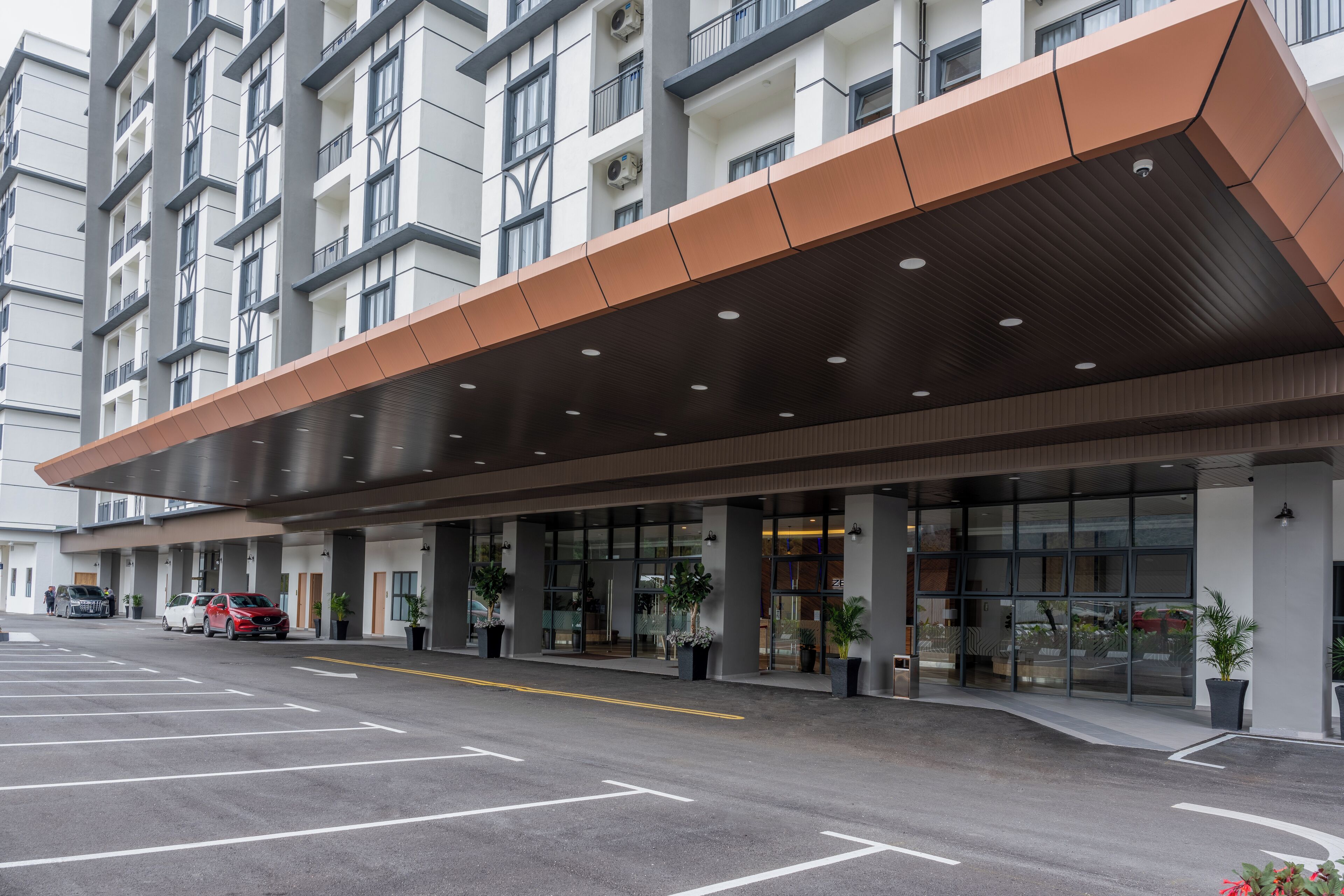 Une entrée d’hôtel moderne avec une allée couverte, des portes en verre et des plantes en pot.