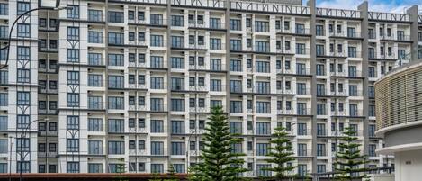 A multi-story residential building with a uniform facade, balconies, and a parking area with cars.