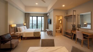 A hotel room with a bed, desk, chair, and a balcony with a view. - Zenith Suites Cameron (Tanah Rata)