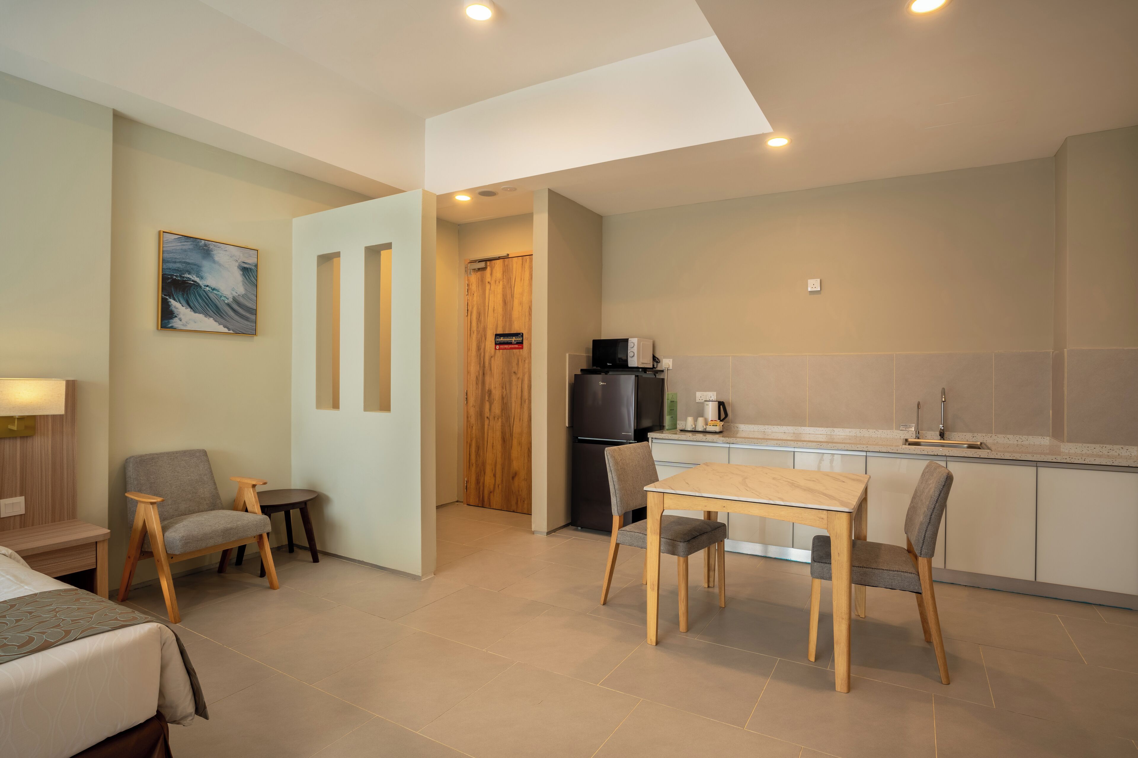 A modern hotel room with a bed, a small desk, a chair, a dining table, and a kitchenette.
