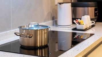 A stainless steel pot on an induction cooktop, a white kettle, and a coffee maker on a kitchen countertop.