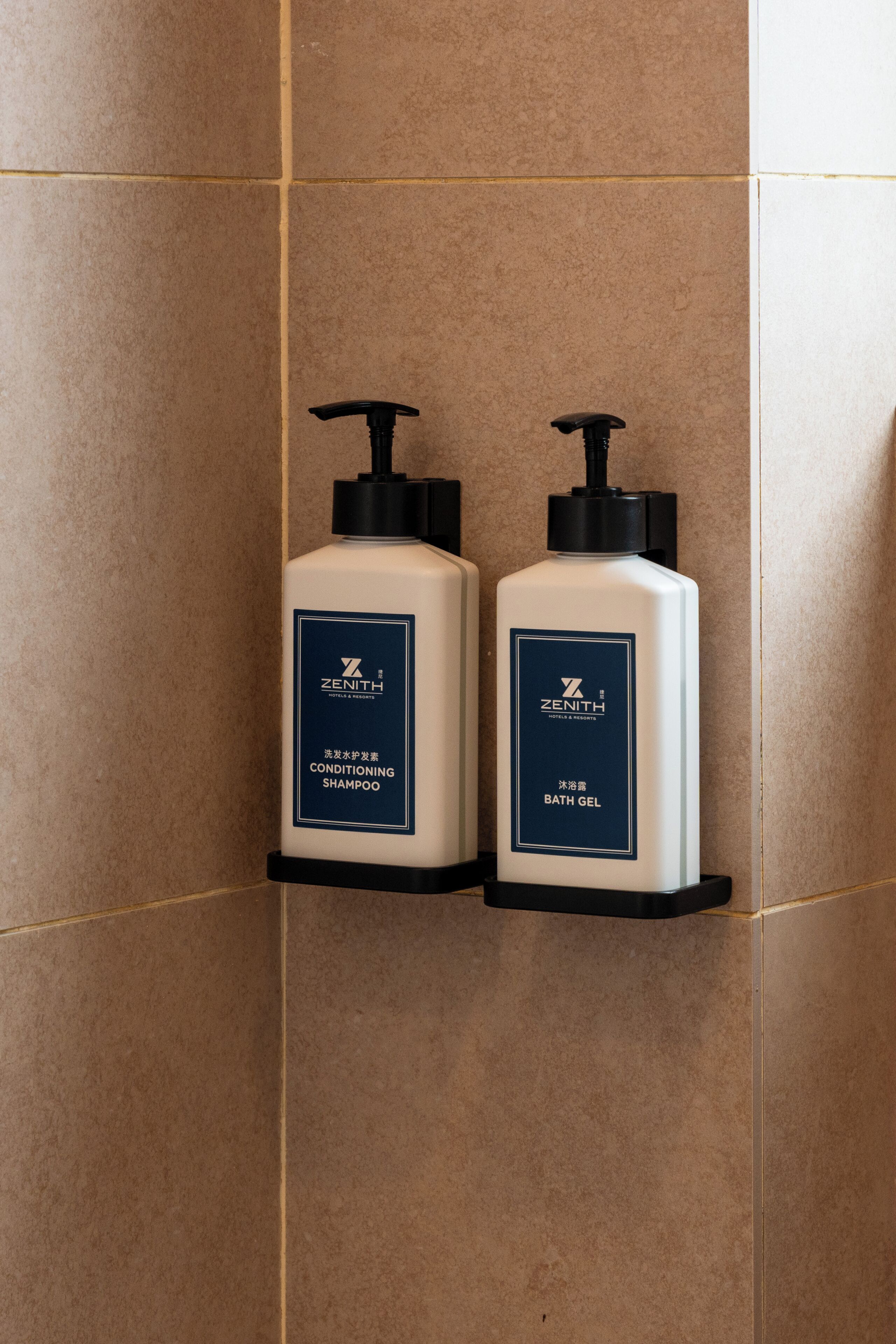 Two bottles of Zenith conditioning shampoo and bath gel on a tiled wall.
