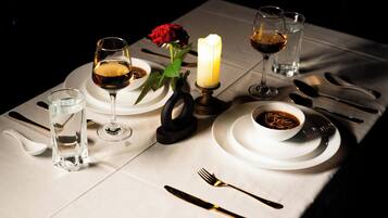 A table set for a meal with wine glasses, a candle, a rose, and a bowl of soup.