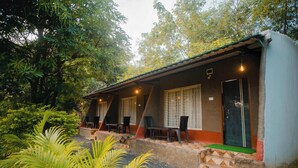 A building with a sloped roof, outdoor seating with tables and chairs, and a door with a window. - Wagharanya Resort (Bhadravathi)