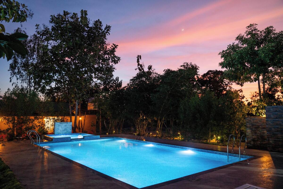 Una piscina rectangular con una zona de borde oscura, rodeada de árboles y un muro de piedra.