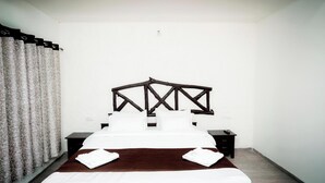 A hotel room with a bed, a headboard, a nightstand, and a curtain. - Wagharanya Resort (Bhadravathi)