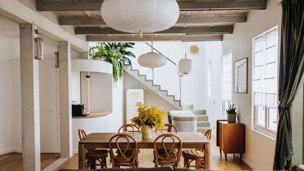 A dining area with a wooden table, wicker chairs, and a vase of yellow flowers. There is a staircase leading to another level, and a potted plant on the wall. - Maison Hubert (Bordeaux)