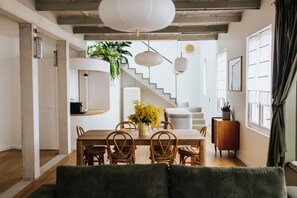 A dining area with a wooden table, wicker chairs, and a vase of yellow flowers. There is a staircase leading to another level, and a potted plant on the wall. - Maison Hubert (Bordeaux)