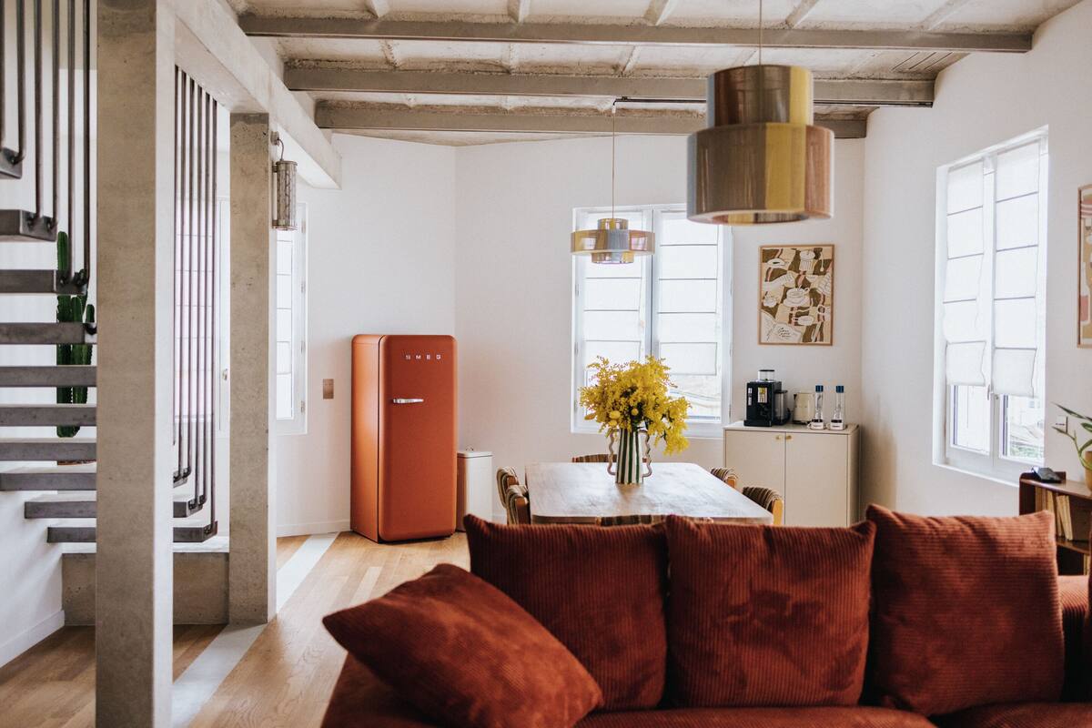 A modern living room with a sofa, a dining table with chairs, a kitchen area, and a staircase.