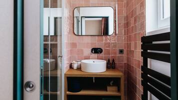 A bathroom with a wooden vanity, a white sink, a mirror, and pink-tiled walls.