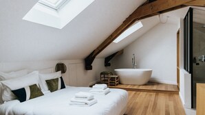 A bedroom with a skylight, a large bed, a bathtub, and wooden flooring. - Maison Hubert (Bordeaux)