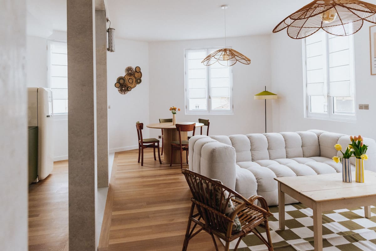 A modern living room with a sectional sofa, a dining table, and a wicker chair.