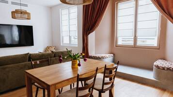 Een moderne woonkamer met een houten eettafel, twee houten stoelen, een bank en een aan de muur bevestigde televisie.