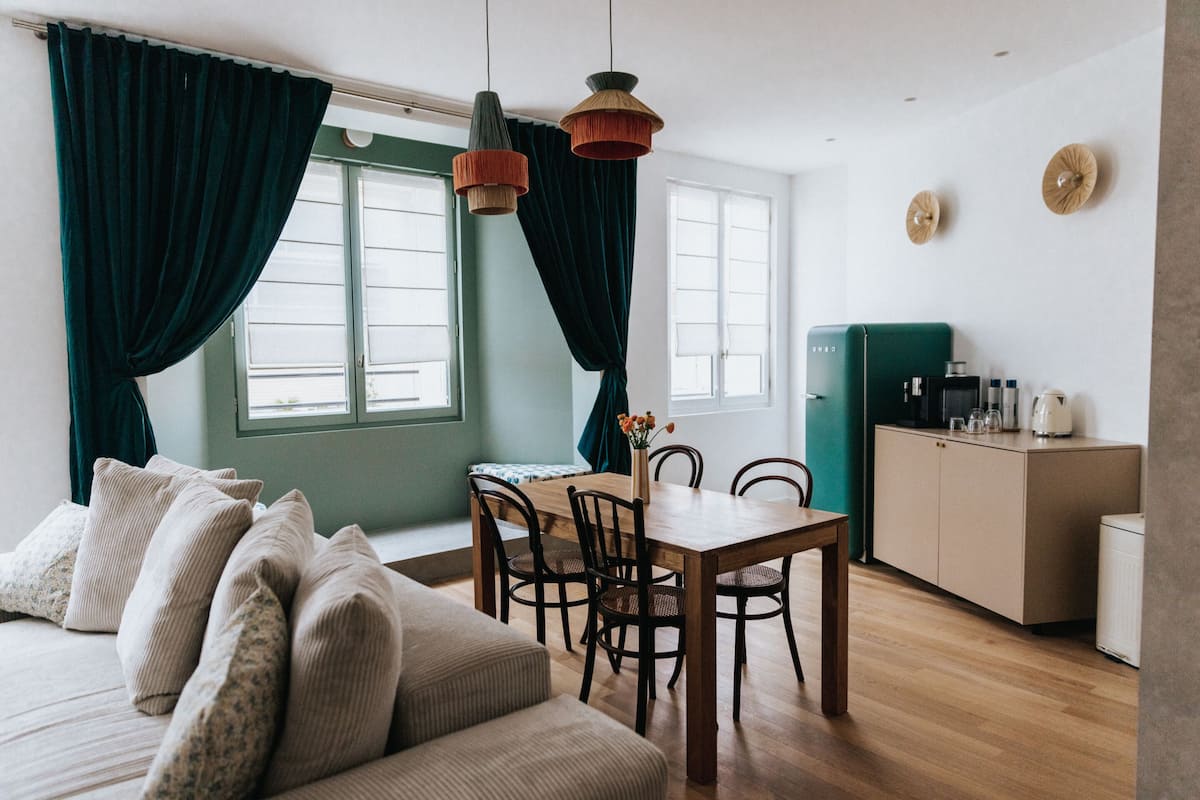 A cozy living room with a sofa, a dining table with chairs, and a kitchen area with a refrigerator and cabinets.