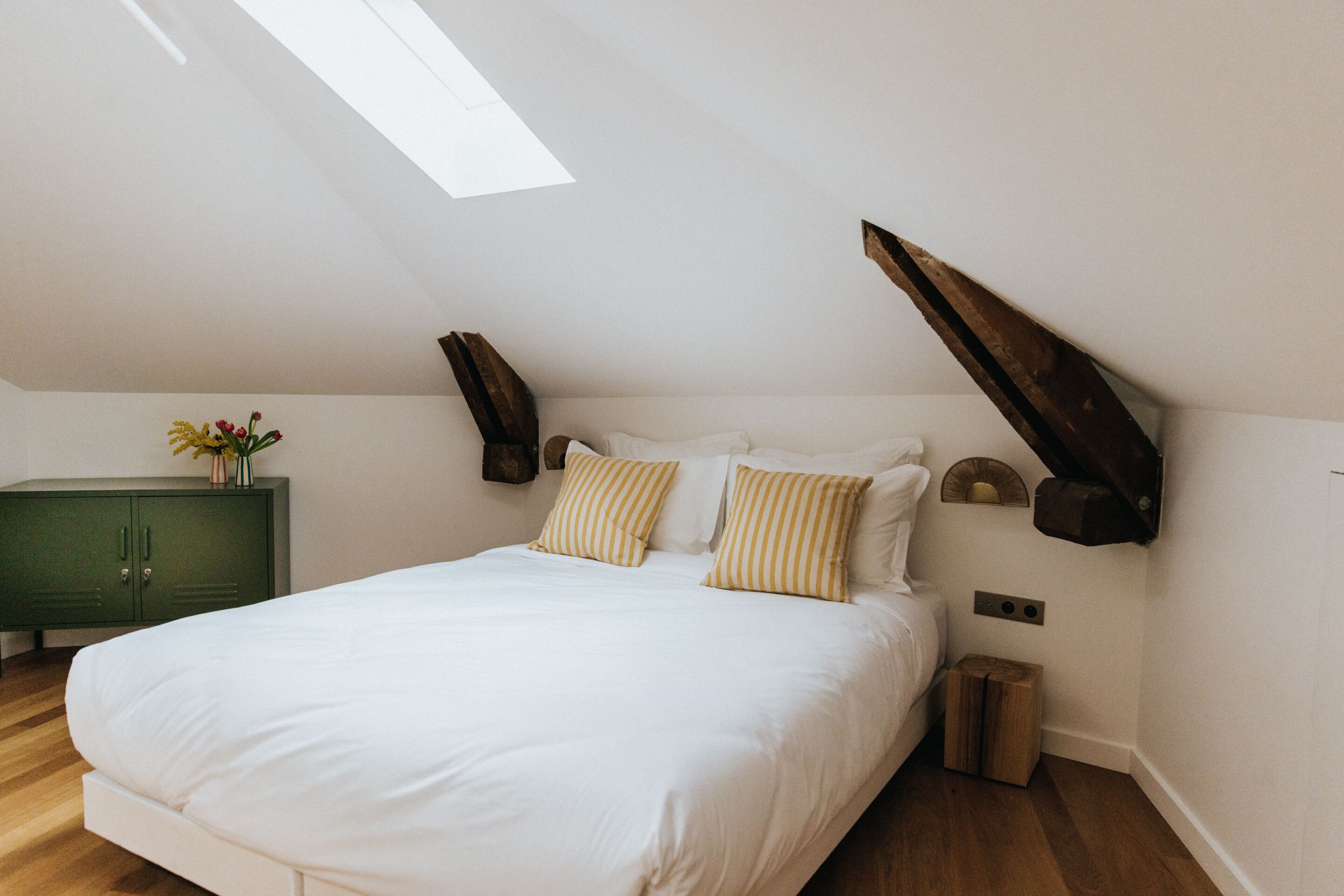Ein Schlafzimmer mit einem großen Bett, Holzbalken, einem grünen Schrank und einem Oberlicht.