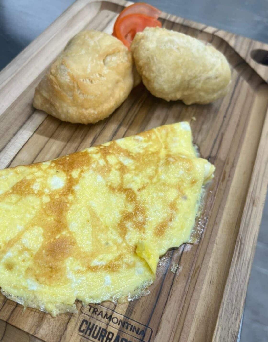 An omelette on a wooden board with two small pastries and a slice of tomato.