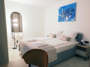 A hotel room with a bed, a chair, a nightstand, and a painting on the wall.