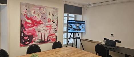 Une salle de conférence avec un grand tableau abstrait, un écran de projection et un ordinateur portable posé sur un bureau.