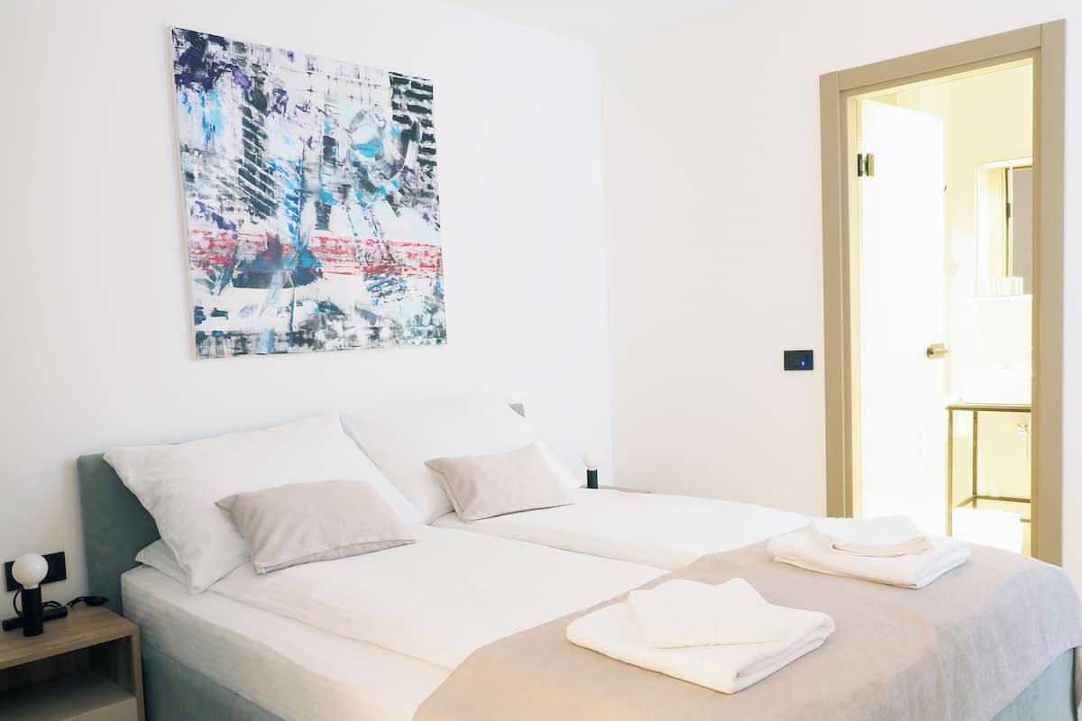 A modern hotel room with a large bed, two bedside tables, a nightstand, and a wall-mounted abstract painting.