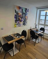 Uma área de refeições com duas mesas, cadeiras pretas e uma grande pintura abstrata na parede.