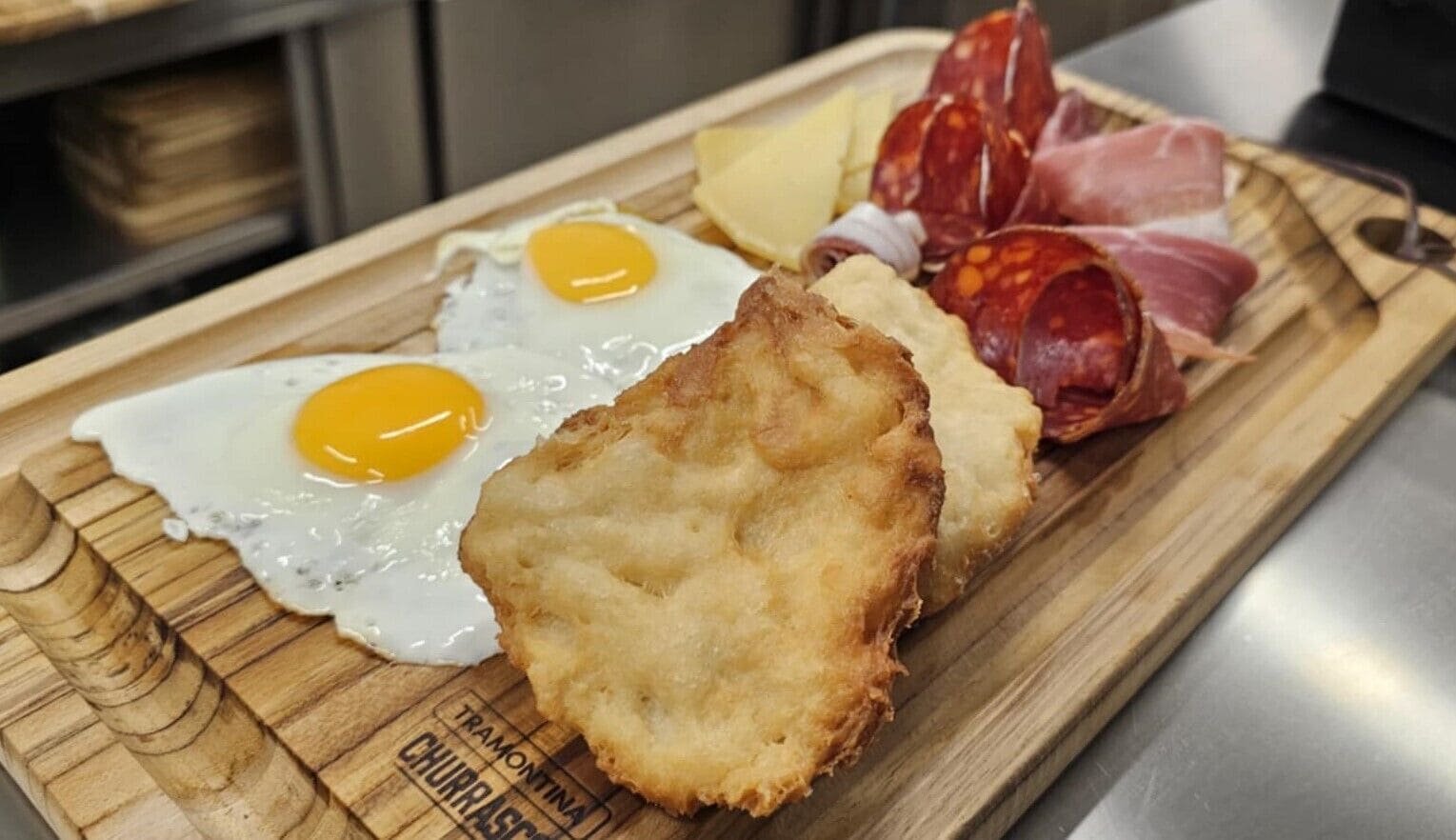 A wooden cutting board with fried eggs, a breaded item, and various meats.