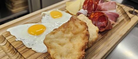A wooden cutting board with fried eggs, a breaded item, and various meats.