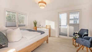 Un dormitorio con cama, mesita de noche, lámpara, silla y vistas al exterior a través de una puerta corrediza.