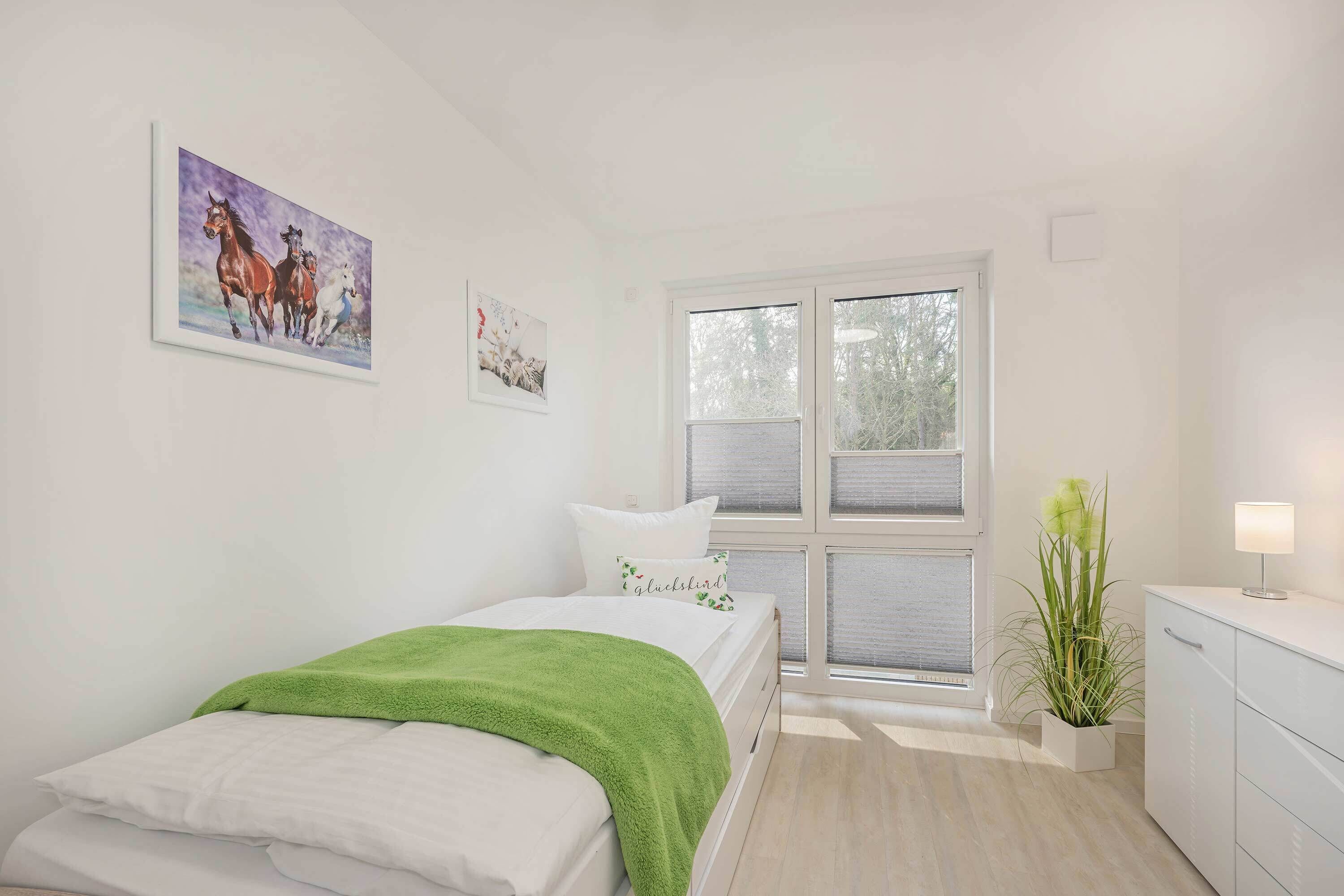 A bedroom with a bed, a window, a plant, and artwork on the wall.
