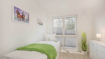 A bedroom with a bed, a window, a plant, and artwork on the wall.
