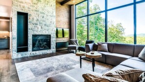 A modern living room with a stone fireplace, large windows, and a cozy seating area.