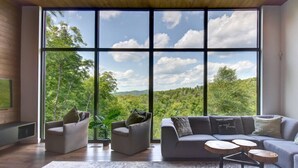 A spacious living room with a large window offering a view of a forested landscape.